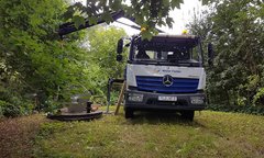 Der Lkw von Walter Fiedler ist in einer grünen Umgebung geparkt, während ein Kranarm bereit ist, eine Last zu heben.