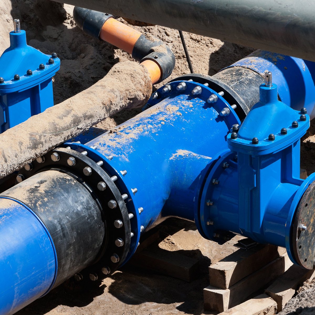 In der Baugrube sind robuste blaue Rohre und Ventile zu sehen, die für die Wasserverteilung vorbereitet werden.